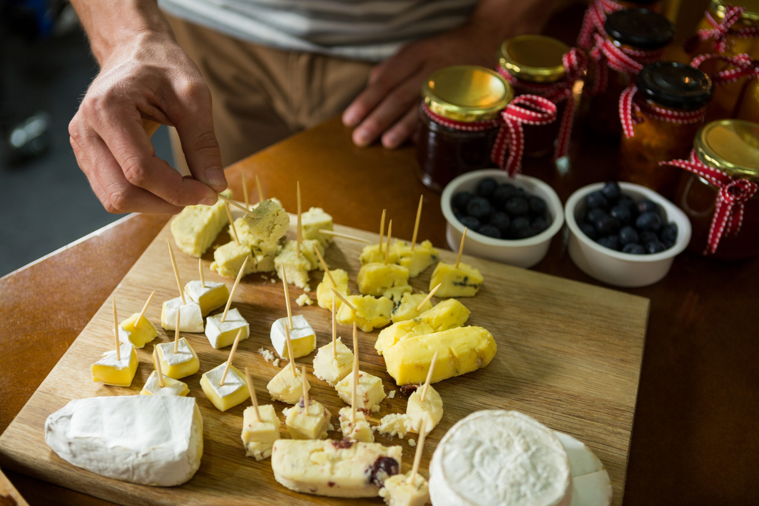 Close-up of staff arranging piece of cheese on wooden board in grocery shop